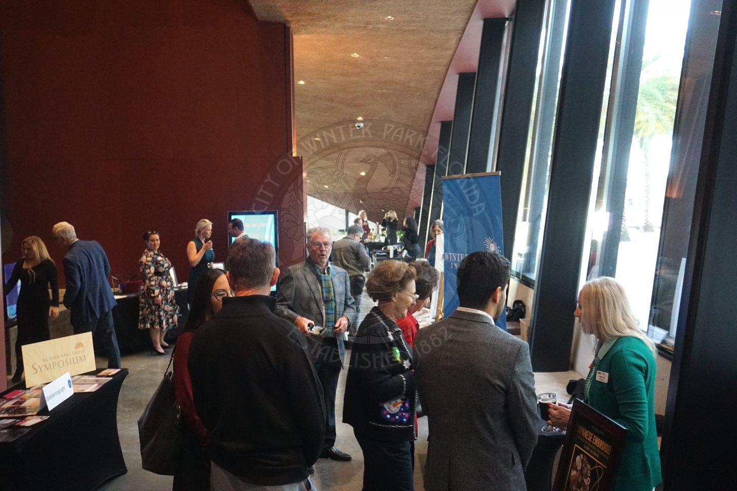 A hallway with vendor tables on both sides and people mingling in the middle with each vendor.