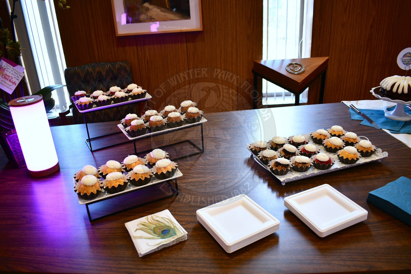 Mini bundtinis on stands for display with a light right next to them and paper plates and napkins in front