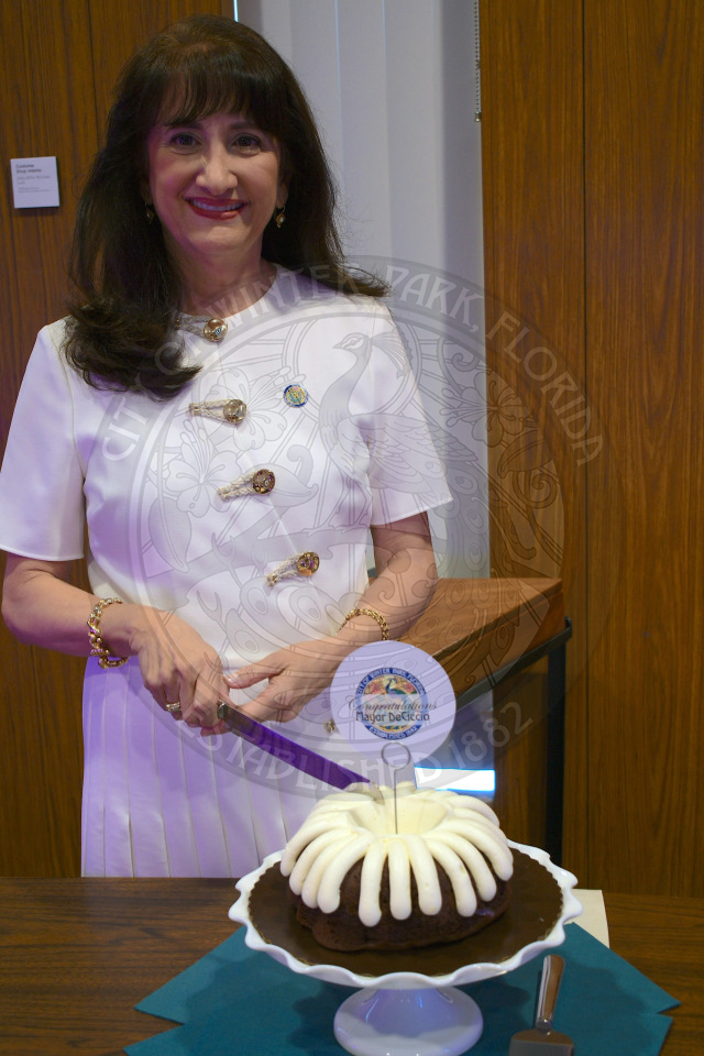 Mayor DeCiccio holding a cake knife cutting into her chocoalte bundt cake and smiling.
