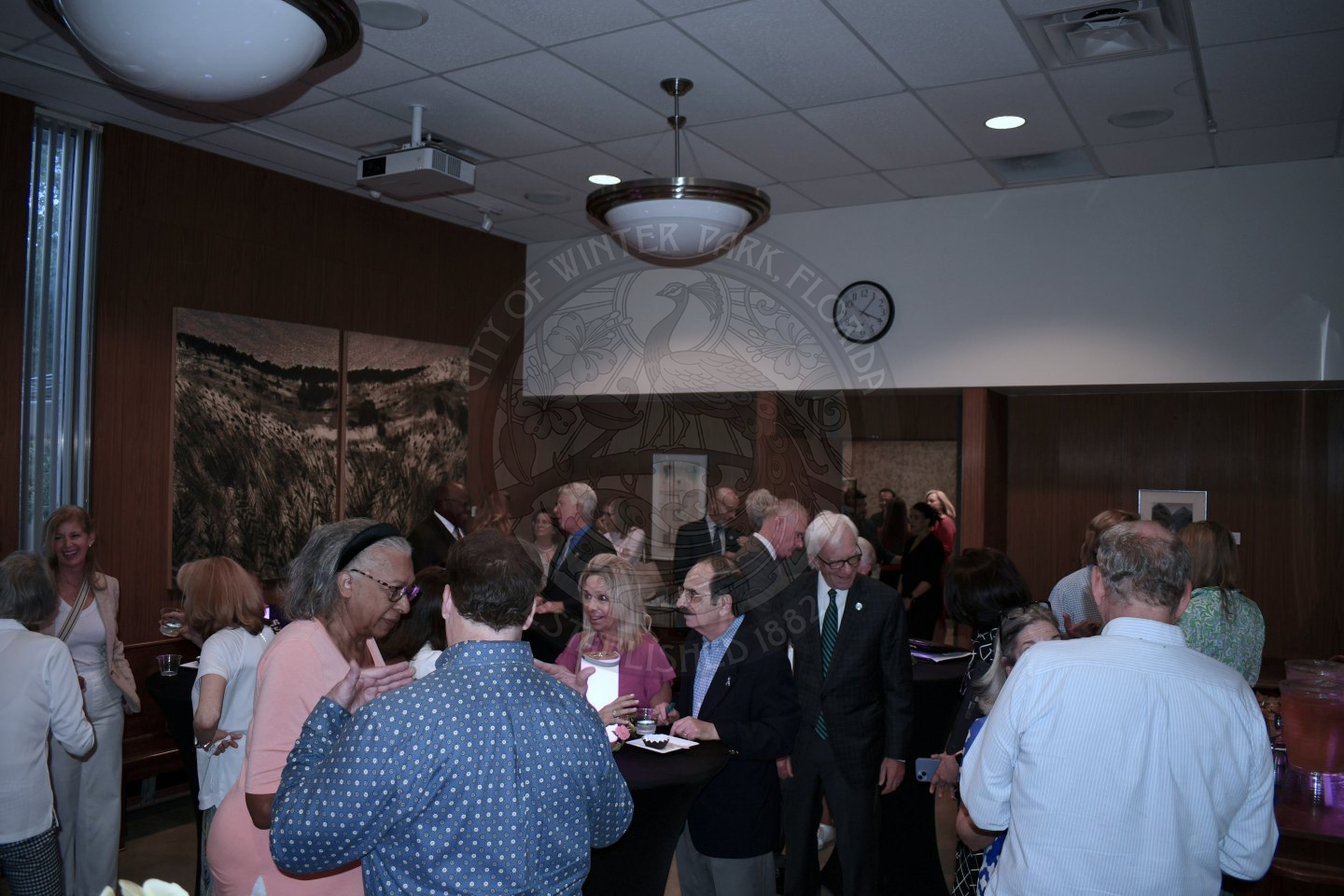 A bunch of people gathered around one another mingling to each other while eating mini bundt cakes and drinking water and punch.