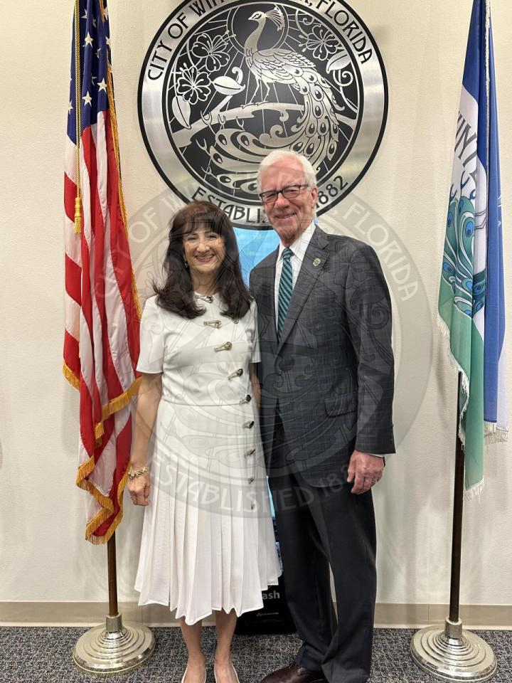 Mayor DeCiccio and Mayor Anderson standing next to each other smiling in front of a metal City Seal hanging on the wall.