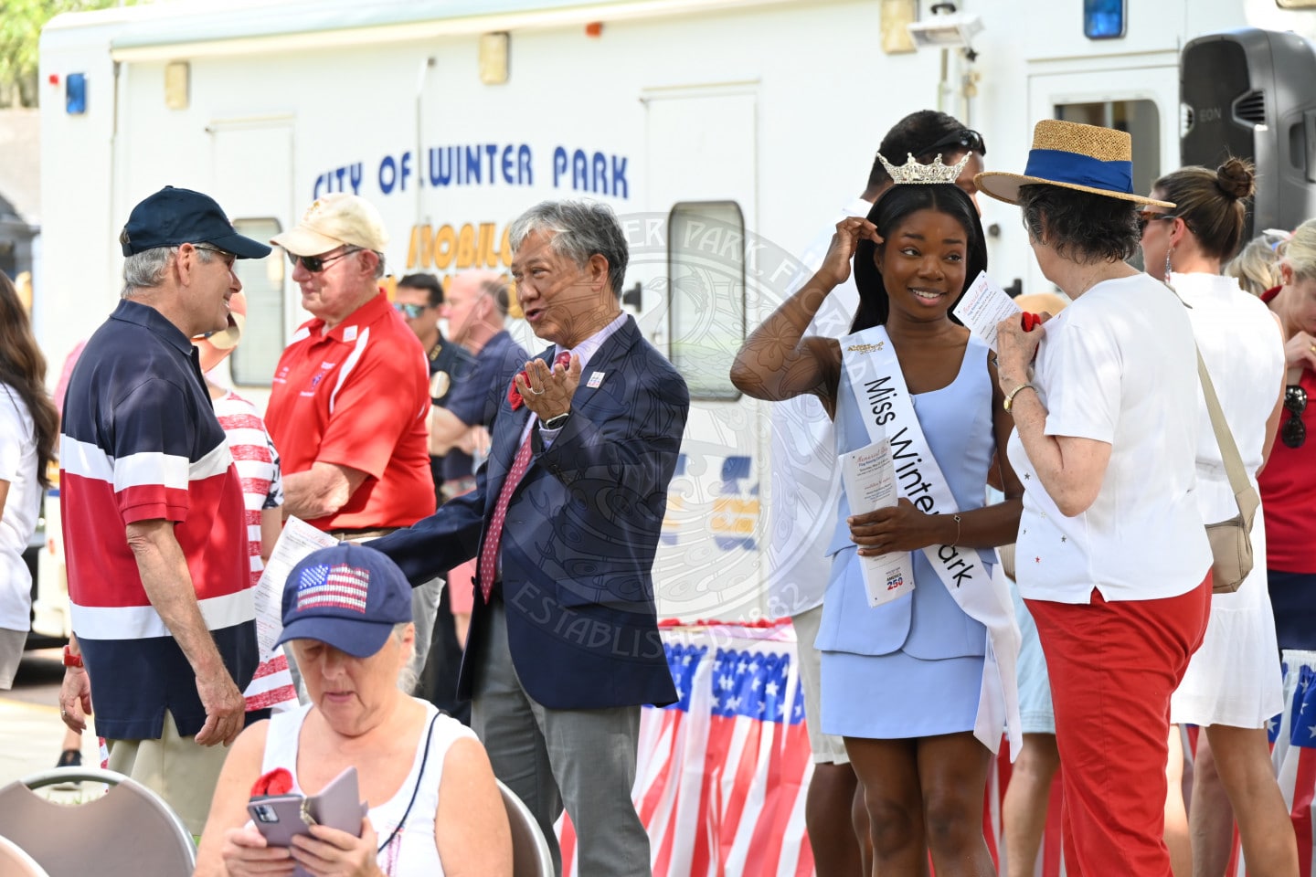 People gather outdoors near a command center truck, many wearing patriotic clothing.