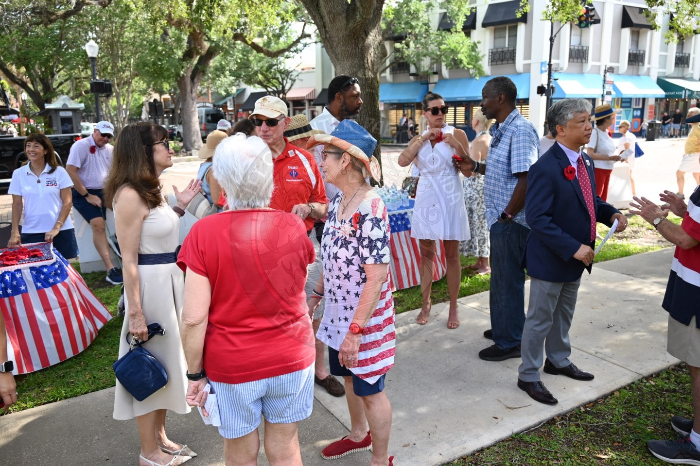 People in patriotic clothing gather and chat outdoors at a festive event, with red, white, and blue decorations.