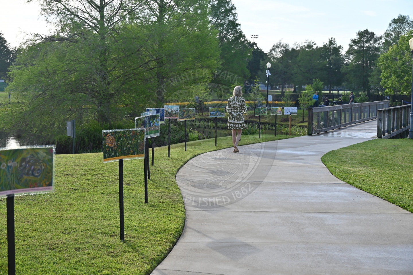 A woman walks along a curved path lined with colorful artwork on display in a park setting.