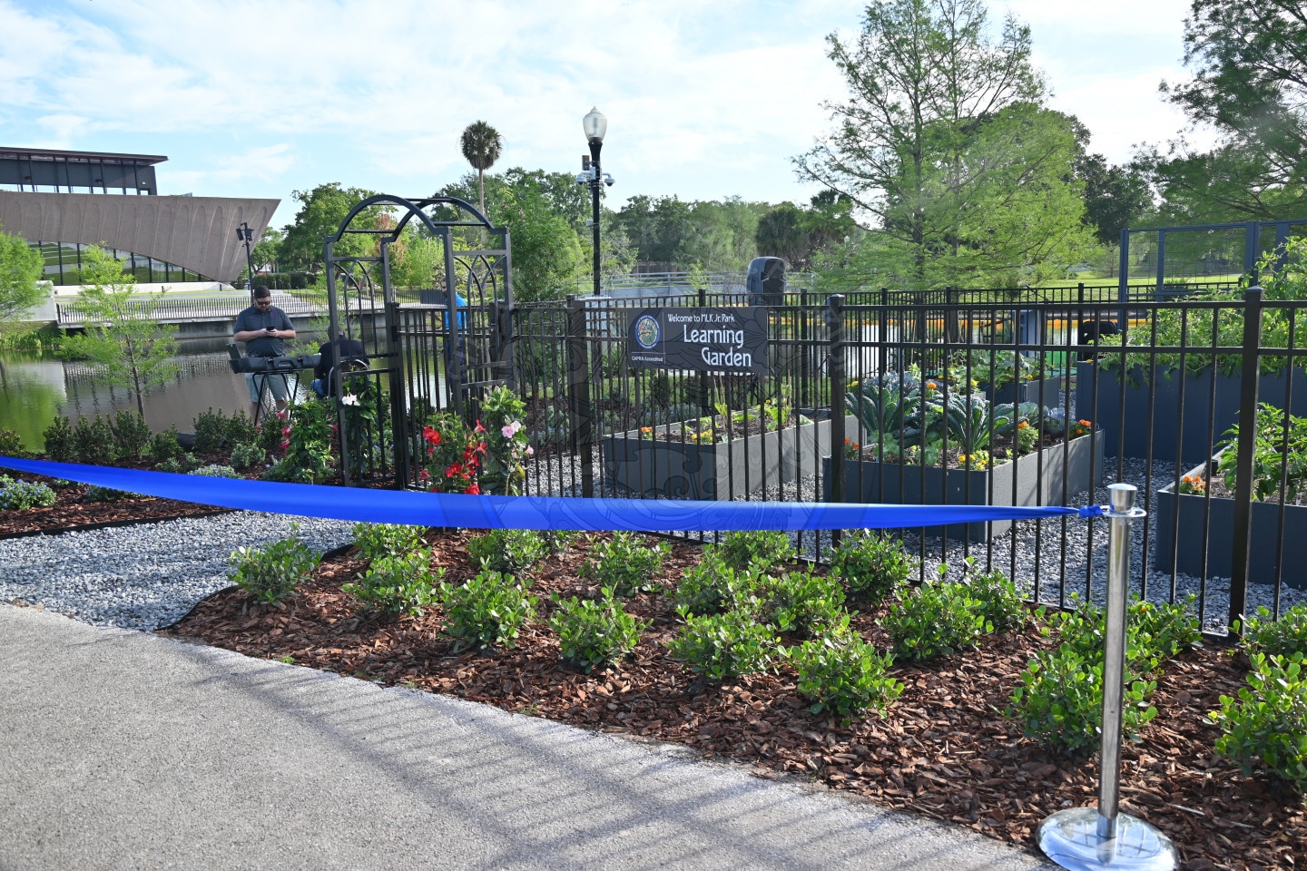 A fenced learning garden with plants, a blue ribbon barrier, and a sign reading Learning Garden.