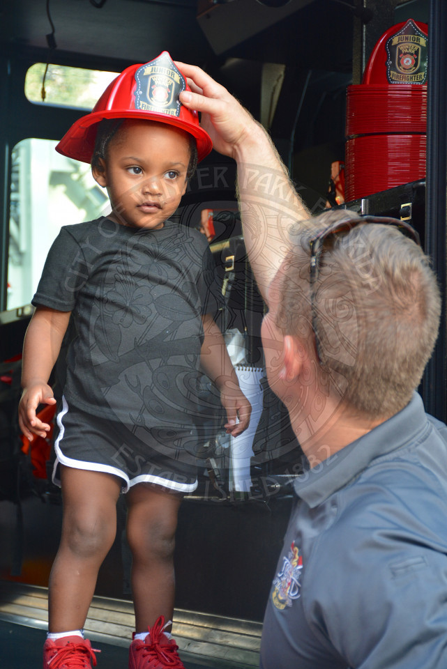 child inside fire truck  with firefighter placing toy helmut on their head