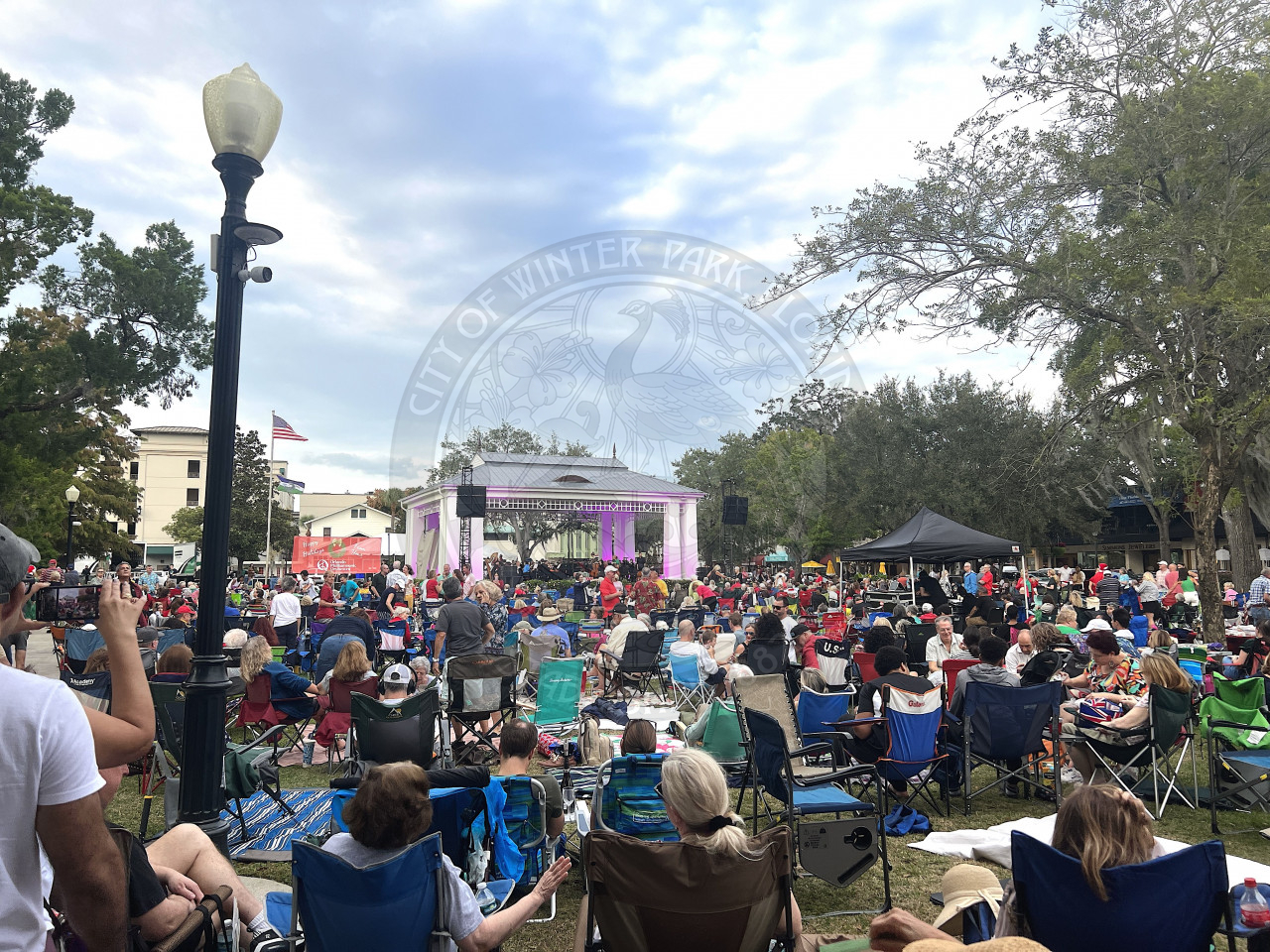 Park filled with people sitting in lawn chairs waiting for the Orlando Philharmonic Orchestra to start playing.