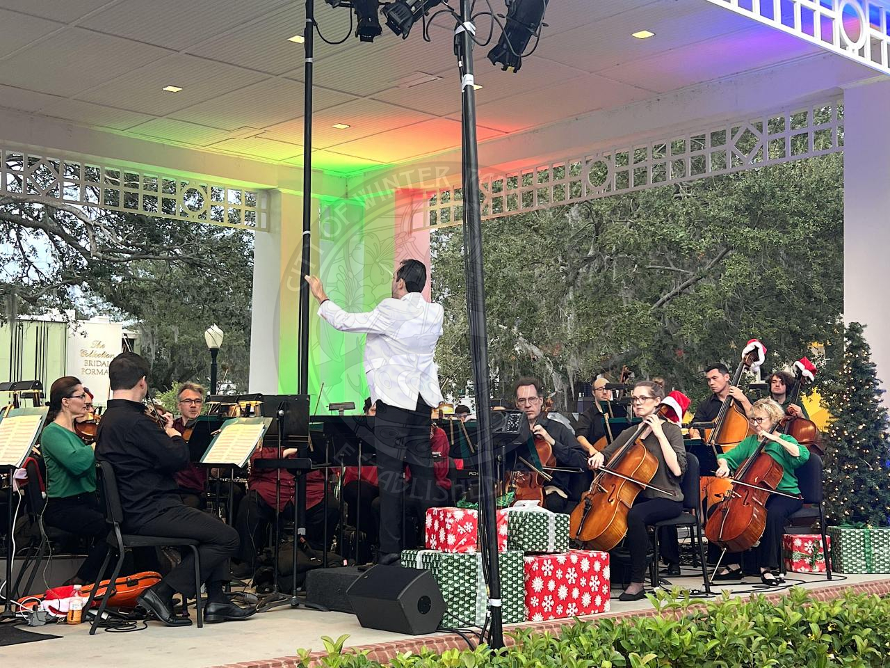 Man standing in front of the stage with his back turned to the crowd conducting a philharmonic orchestra  with green and red lights.