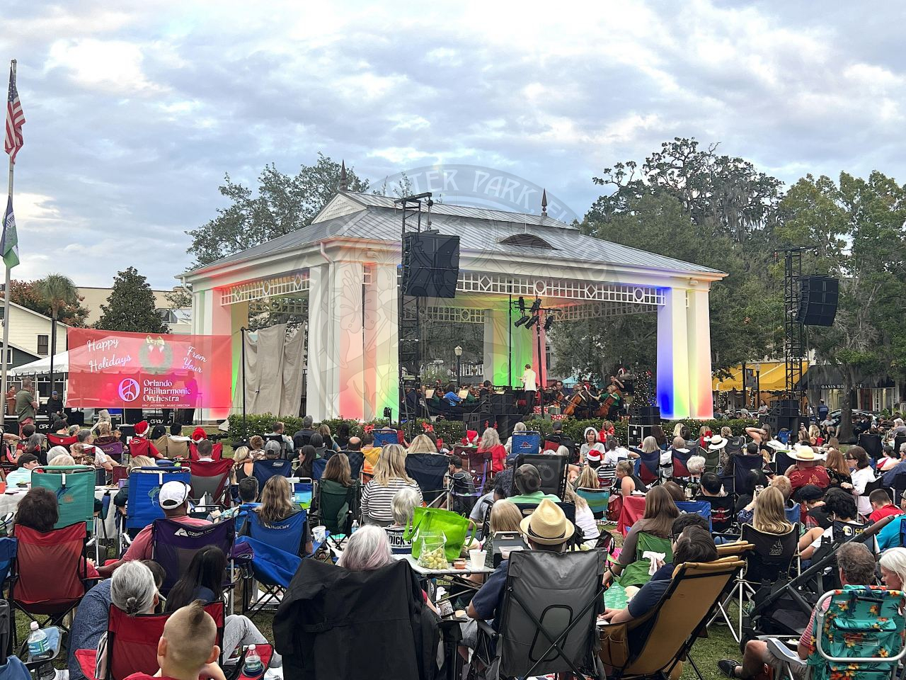Man standing in front of the stage with his back turned to the crowd conducting a philharmonic orchestra 