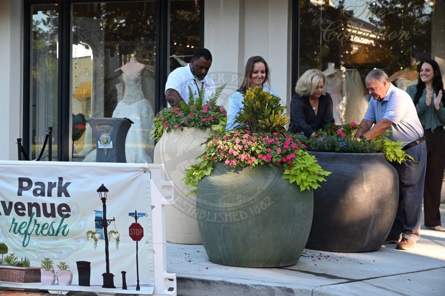 A group of people planting flowers in large decorative pots outside a boutique storefront.