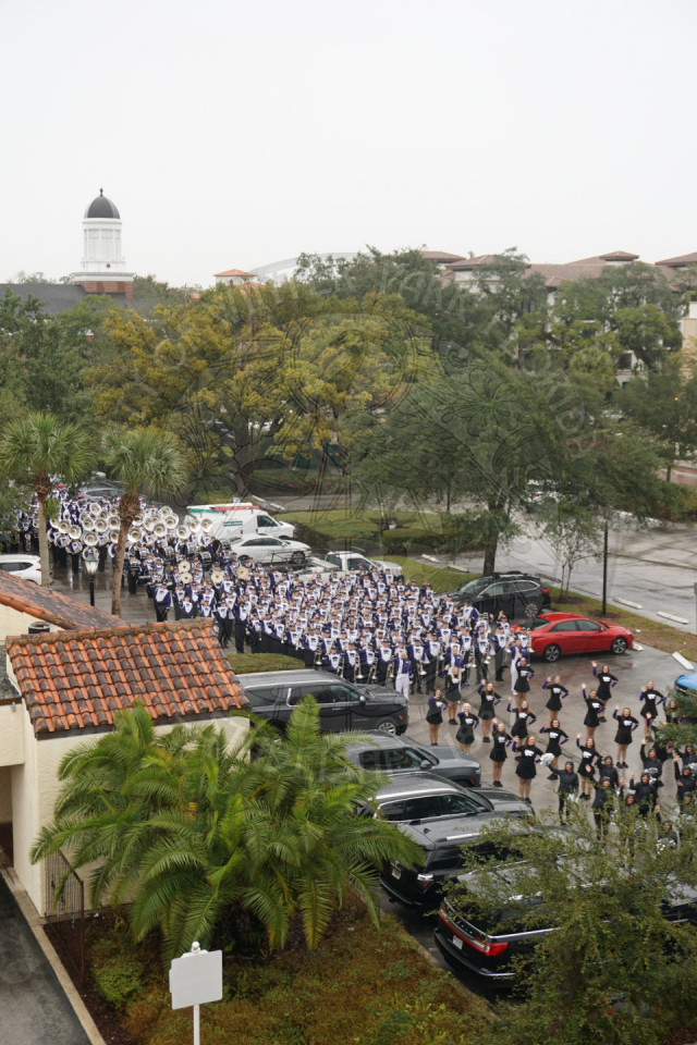 An ariel view of Kansas State band lined up in a parking lot ready to start marching a waving to the camera