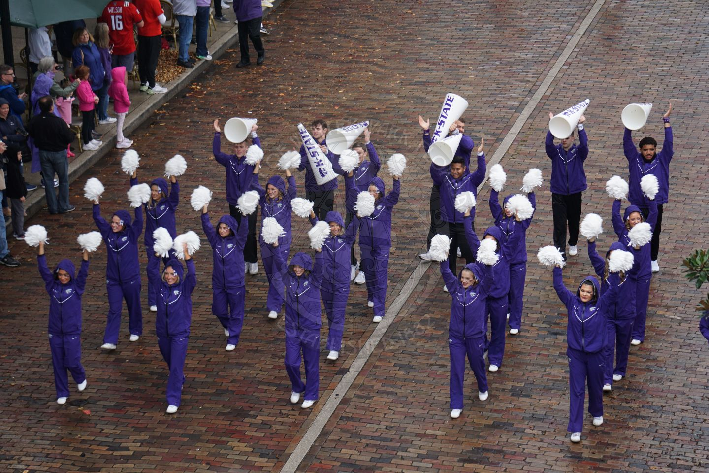 Kansas State cheerleaders marching down Park Avenue in rain coats with the hoods on due to light rain.