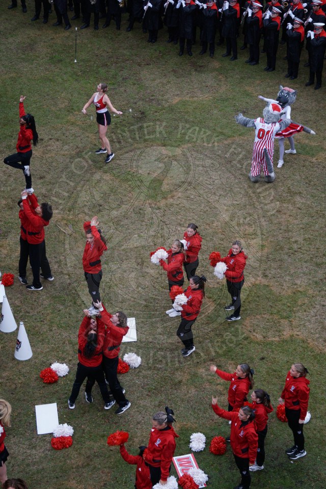 North Carolina cheerleaders are cherring with a baton twirler behind them throwing up a baton. Behind the baton twirler is Mr. and Mrs. Wolf mascots dancing