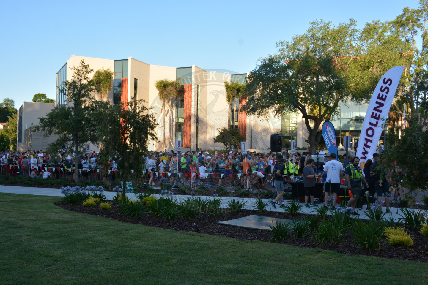 Runners gathering to start the race. Feather banner sign on right with the word Wholeness printed on it.
