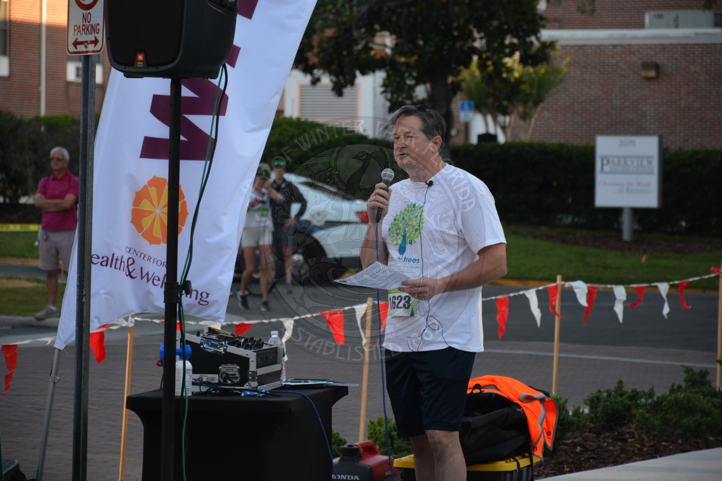 Close up photo of Vice Mayor Greg Seidel offering welcome remarks holding a microphone, next to race signs