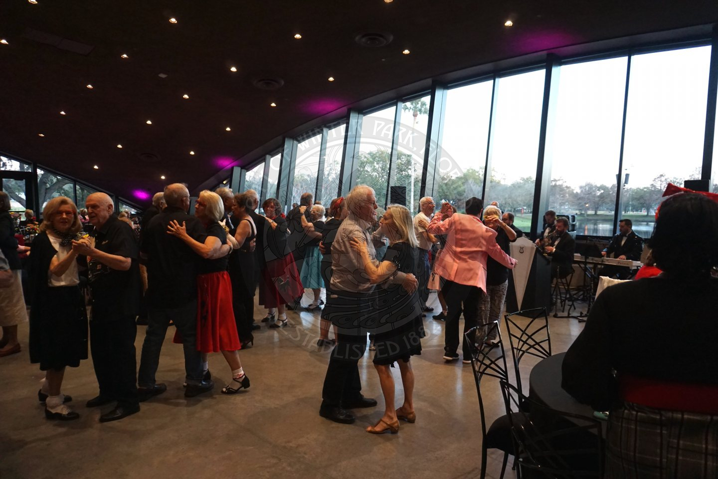 Paired up seniors dancing in the middle of the ballroom to some music.
