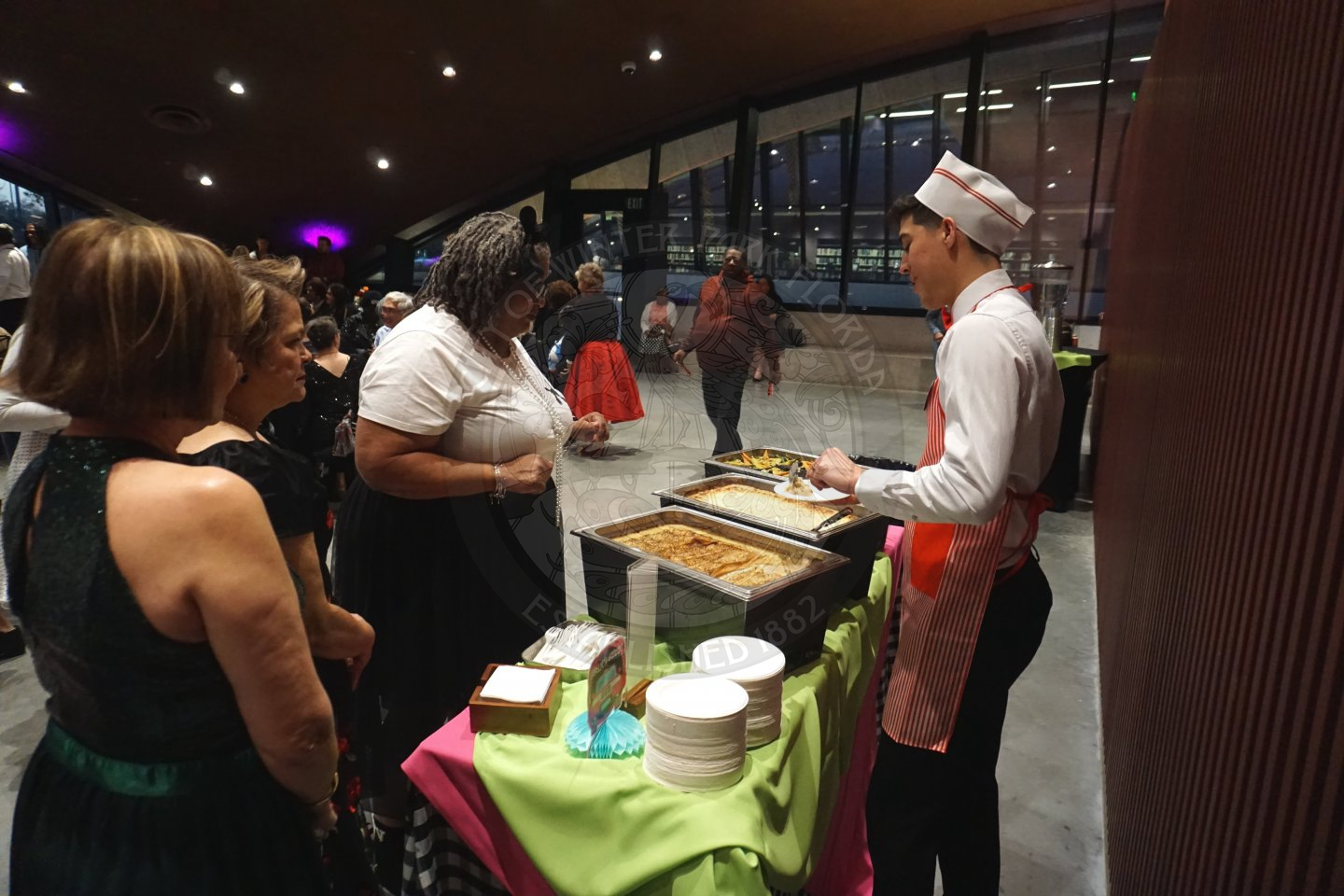 an eating stations with seniors lined up getting served their dinner at prom.