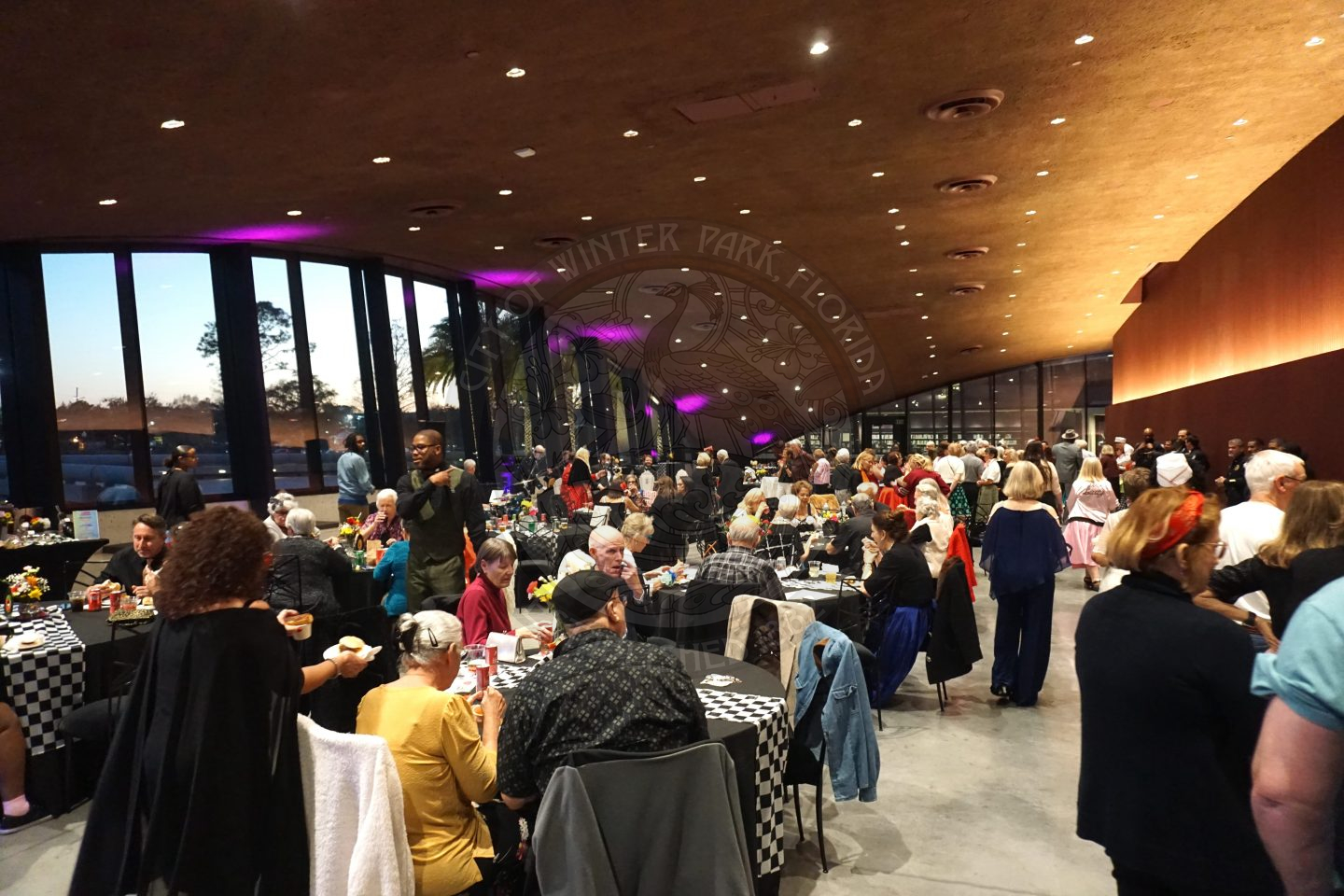 Overview of ballroom with people sitting at tables, getting food, and dancing.