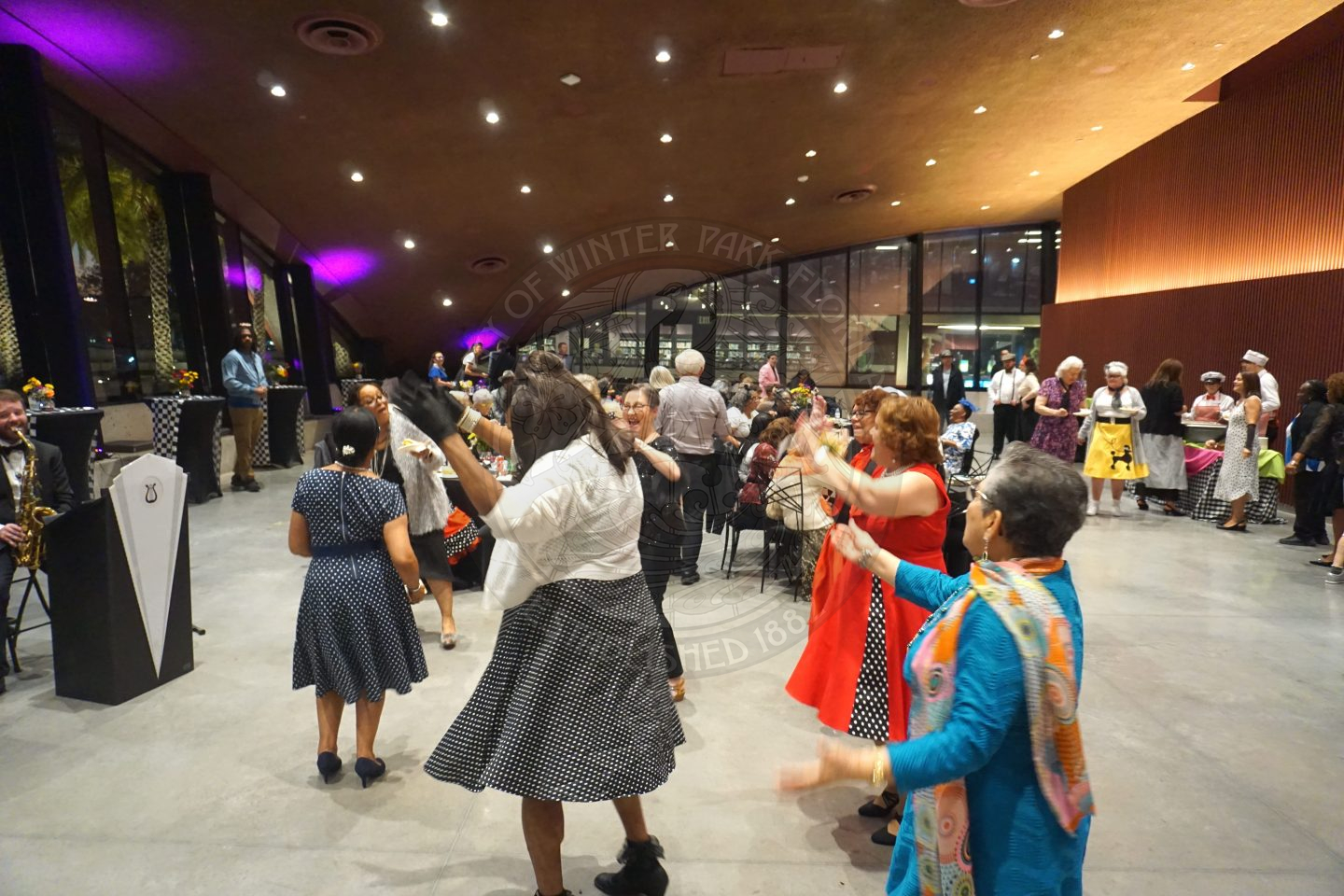 Seniors dancing in the center of the ballroom with tables behind them and senior sitting down.