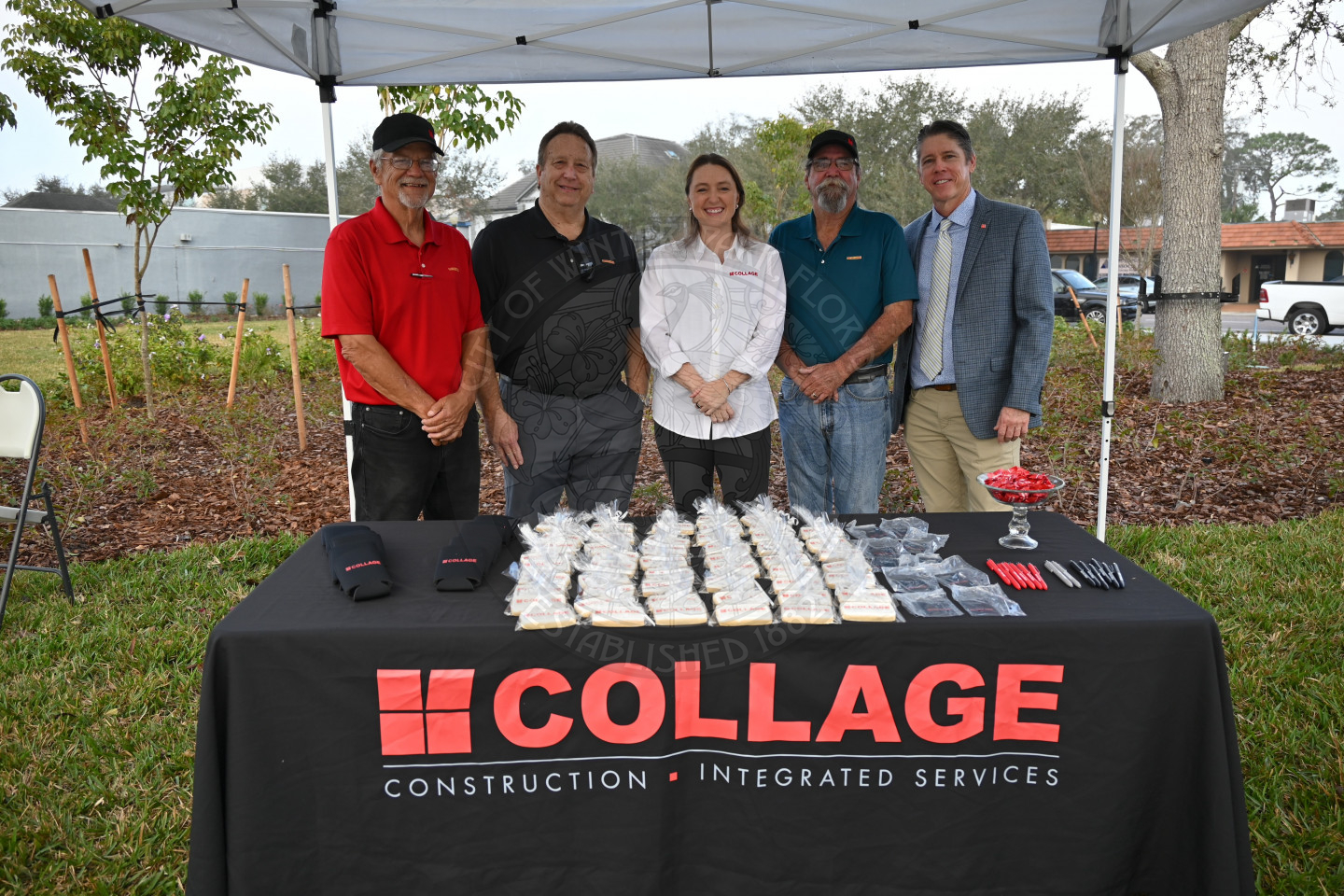 a group of five people standing behind a table with cookies and promotional items for their comapny Collage.
