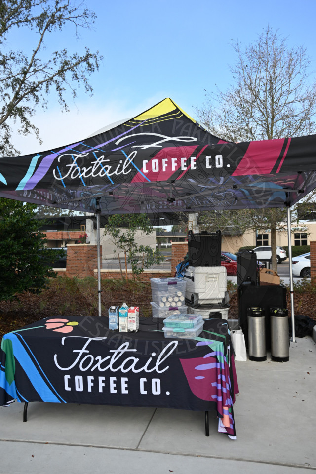 A tent with the Foxtail Coffee Co. logo with a table and coffee canisters on the table,
