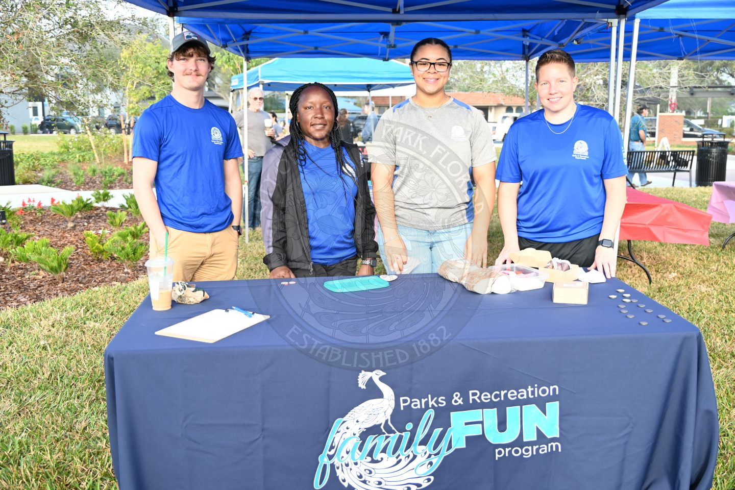 A group of people standing behind a table with a tablecloth on it that says 'Parks &amp; Recreation FUN Program"