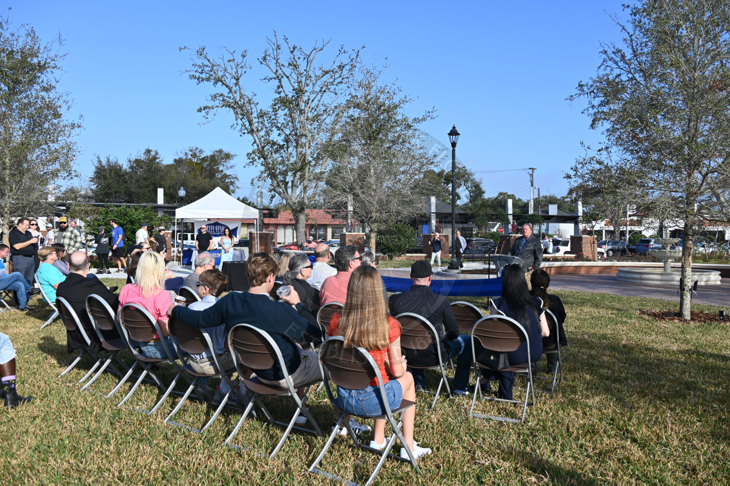 People sitting down in chairs lsitening to a man talking into a mircophone.