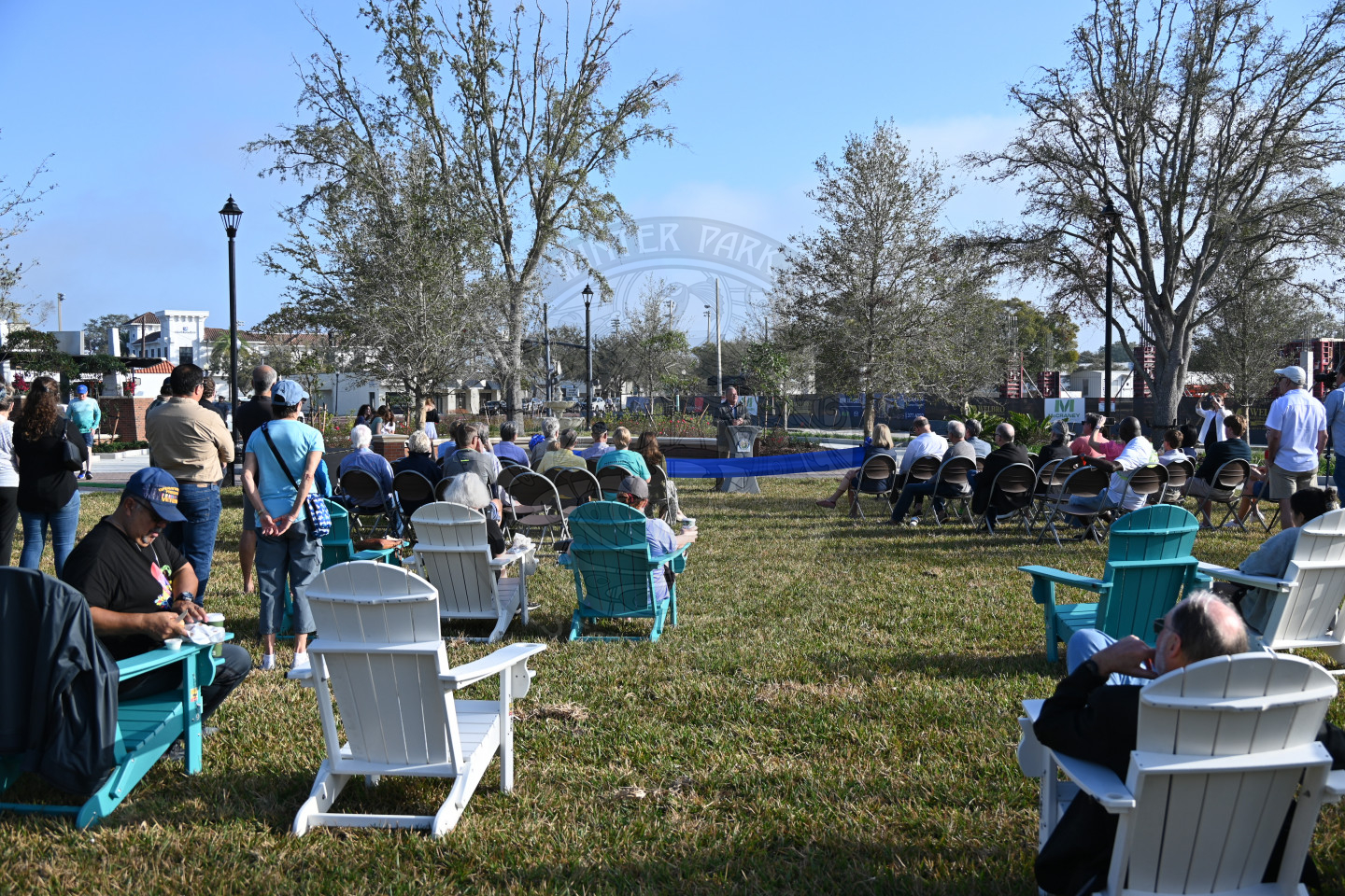 People sitting down in chairs lsitening to a man talking into a mircophone.