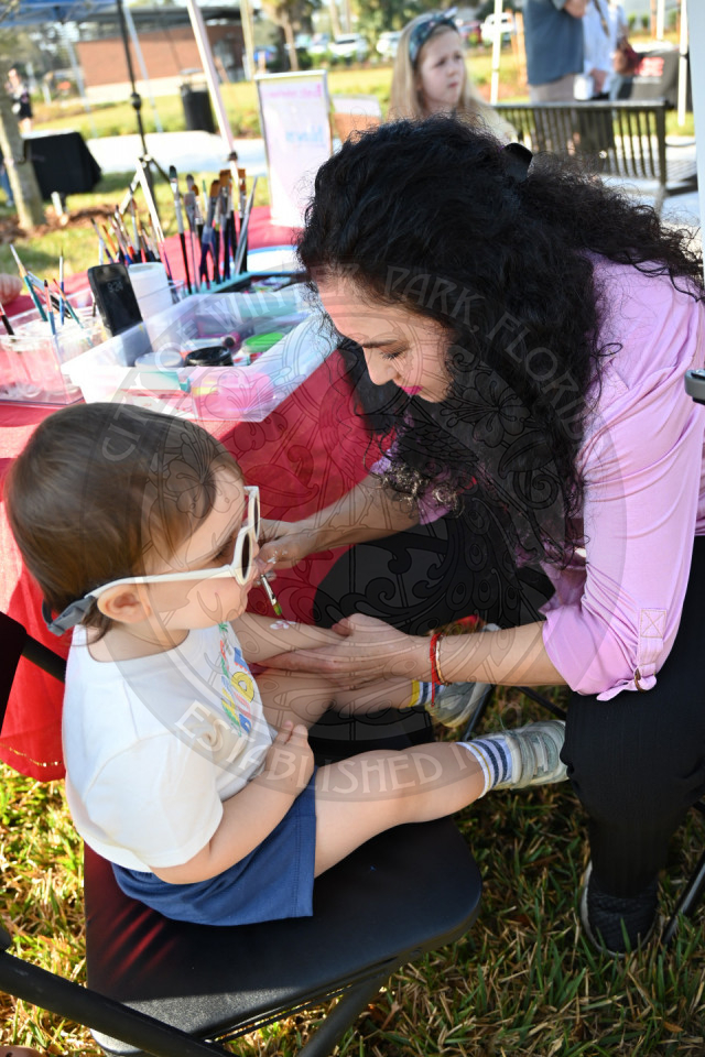 a woman painting a design on a kids arms. 