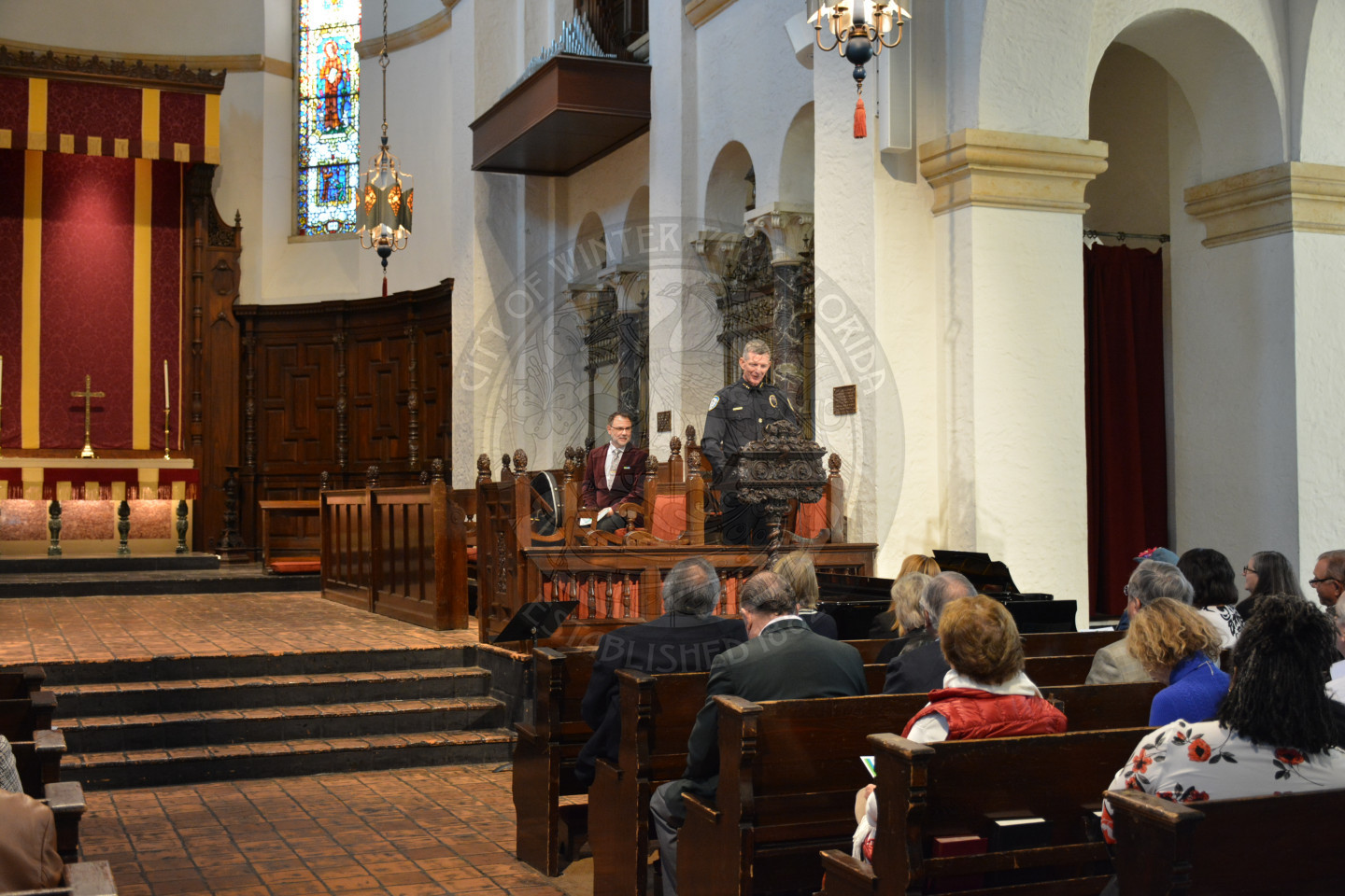 wide shot of Police Chief Deal at the podium while attendees sitting in pews listen to his remarks