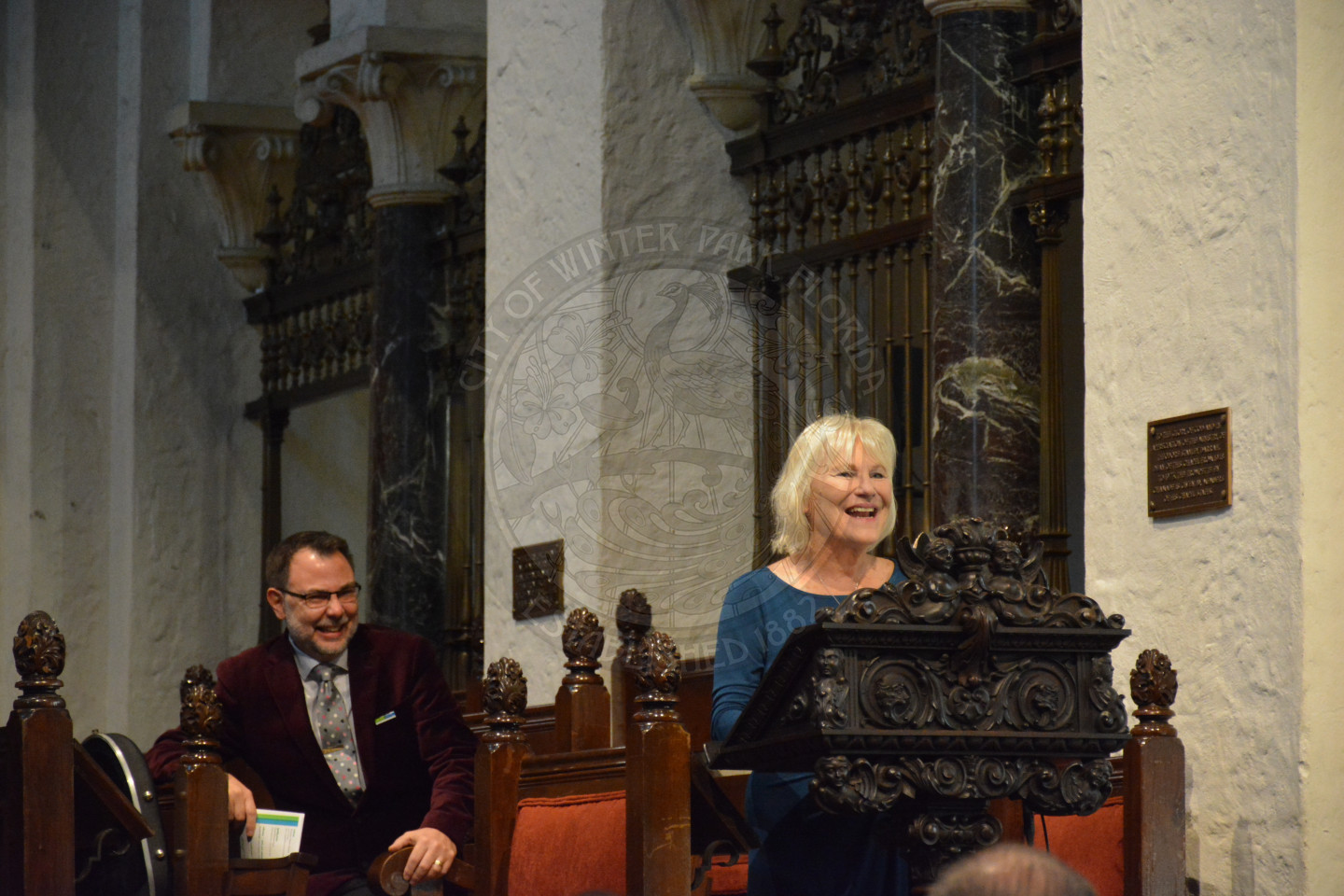 Commission Sarah Sprinkel sharing remarks at the podium. Reverend Shawn Garvey smiling behind her.