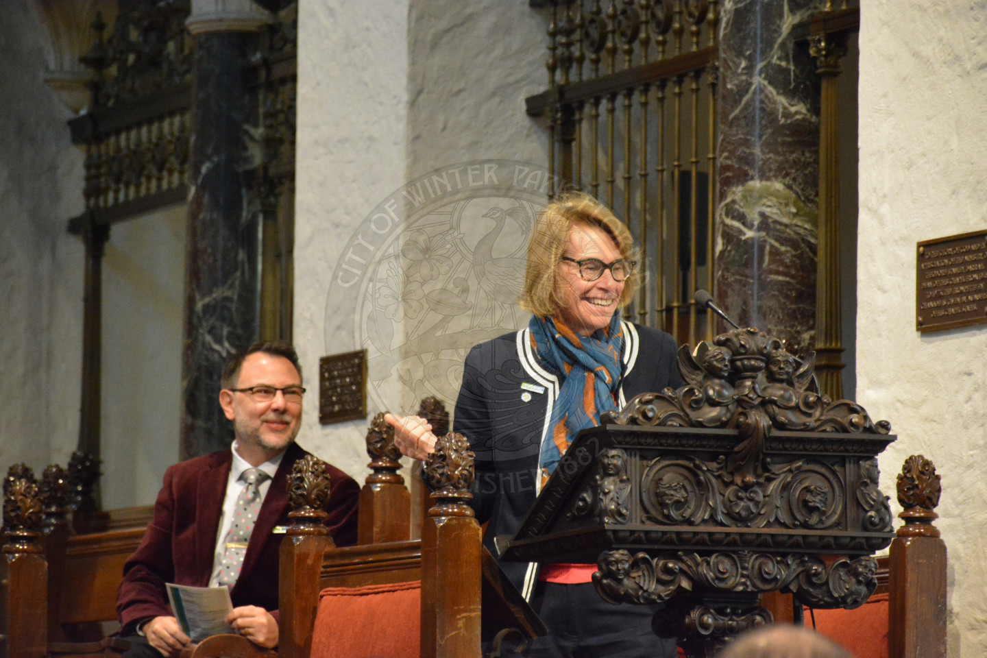 Peg Cornwell of Rollins College sharing remarks at the podium. Reverend Shawn Garvey smiling behind her.