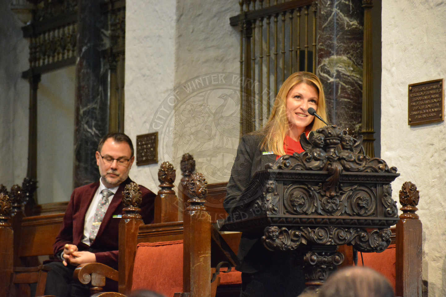 Charlene Hotaling sharing remarks at the podium. Reverend Shawn Garvey sitting behind the podium
