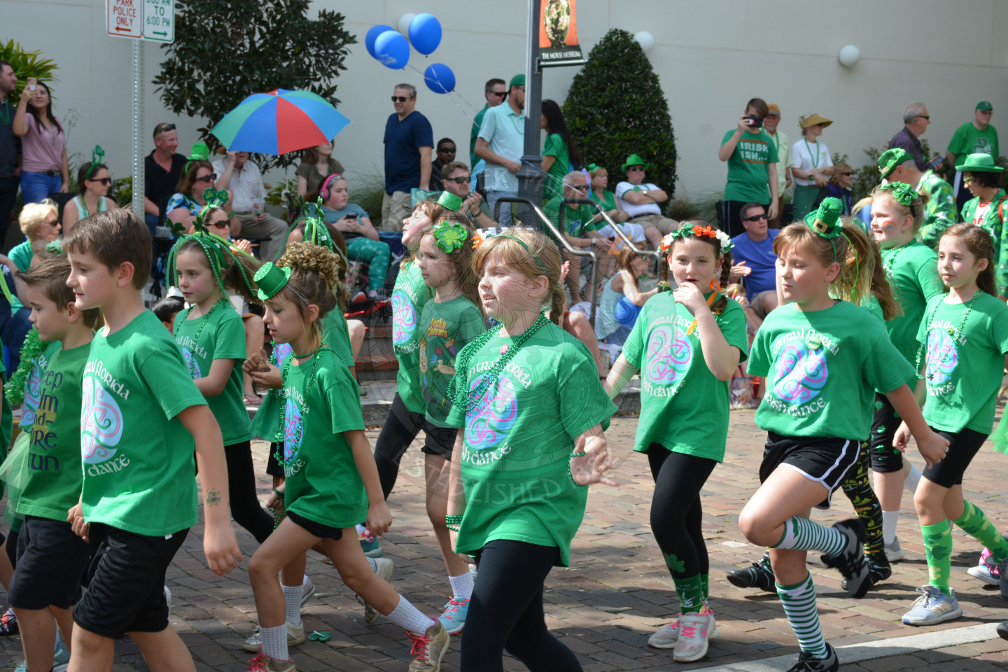 Many young children in festive t-shirts walking down parade route