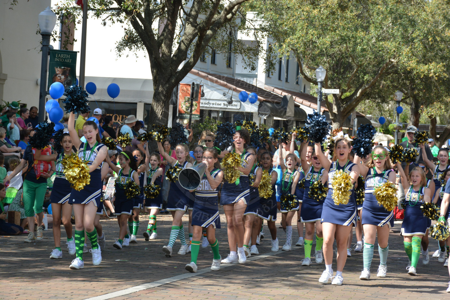 Cheerleaders waving and walking down the parade route holding megaphones and pom poms