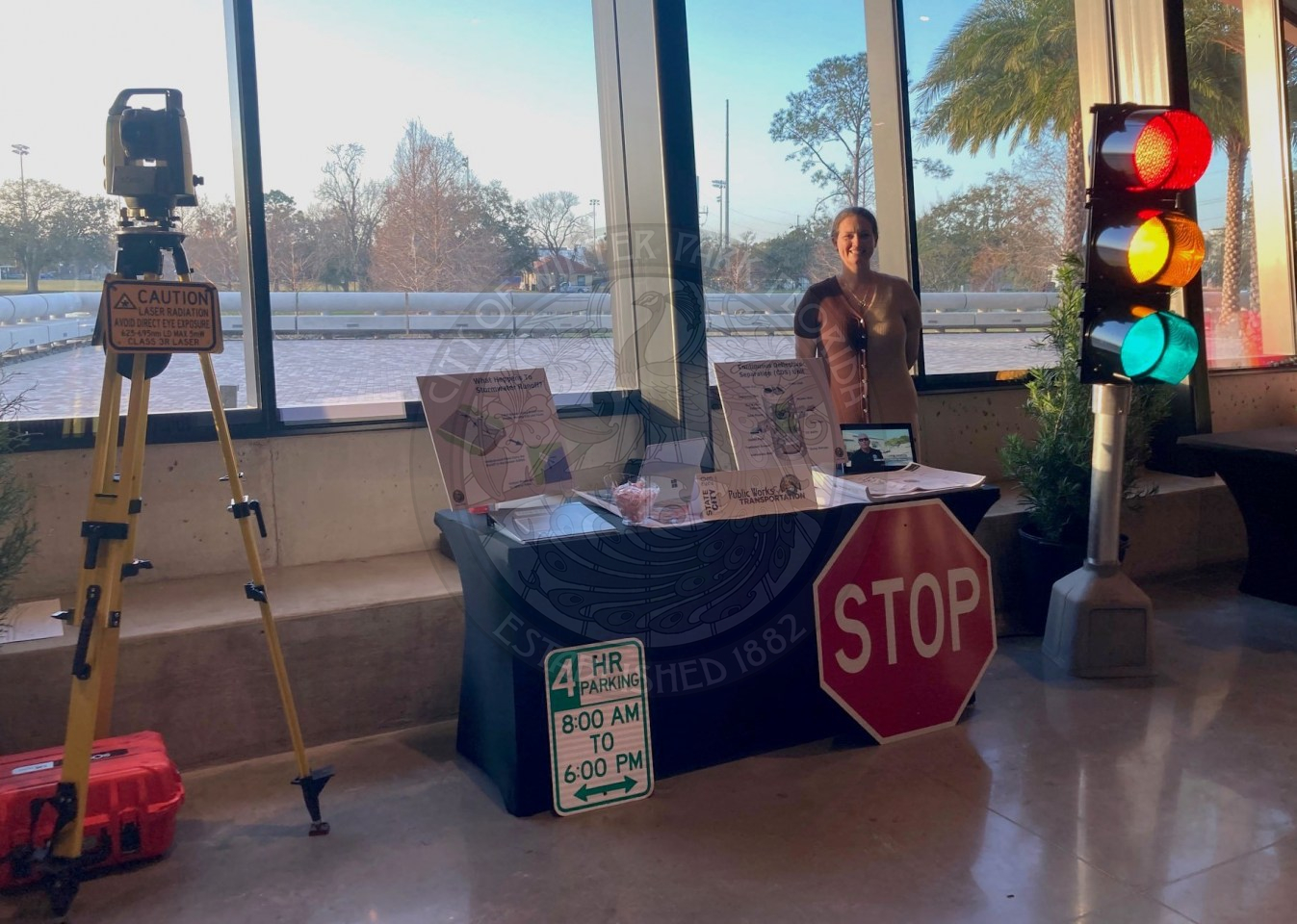 Public Works &amp; Transportaion departmetn table with woman standing behind the table. There is a traffic light to the right of the table and a camera with