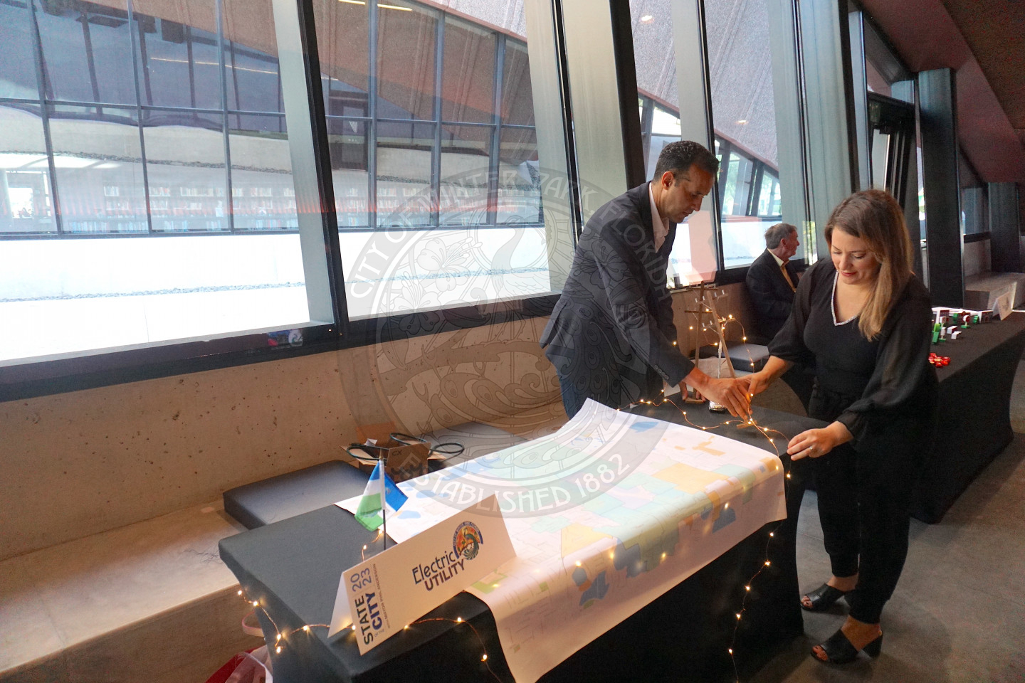 a man and a woman wrapping lights around a table that has a map on it to decorate it.