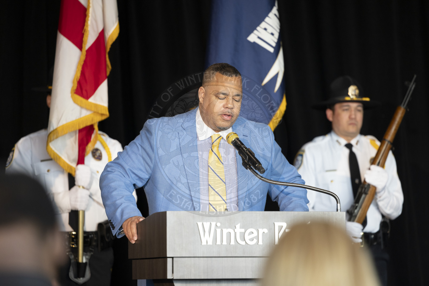 Man standing behind the podium while saying a prayer in front of the group.
