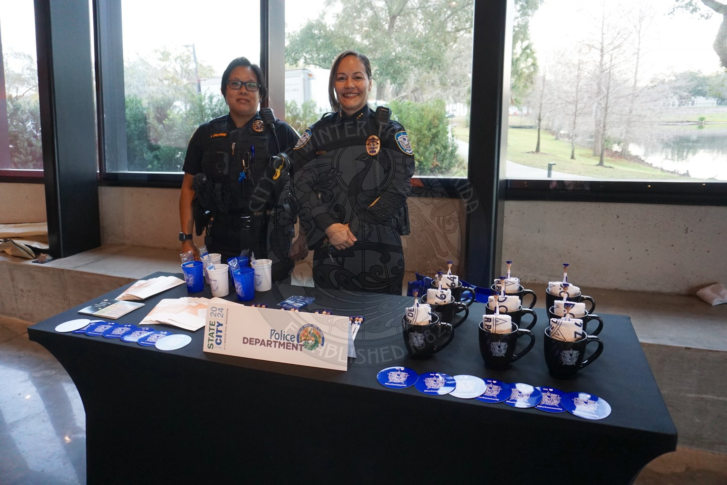Two officers standing behind a table that has Winter Park Police Deparmtent promotional items such as mugs, magnets and cups. 