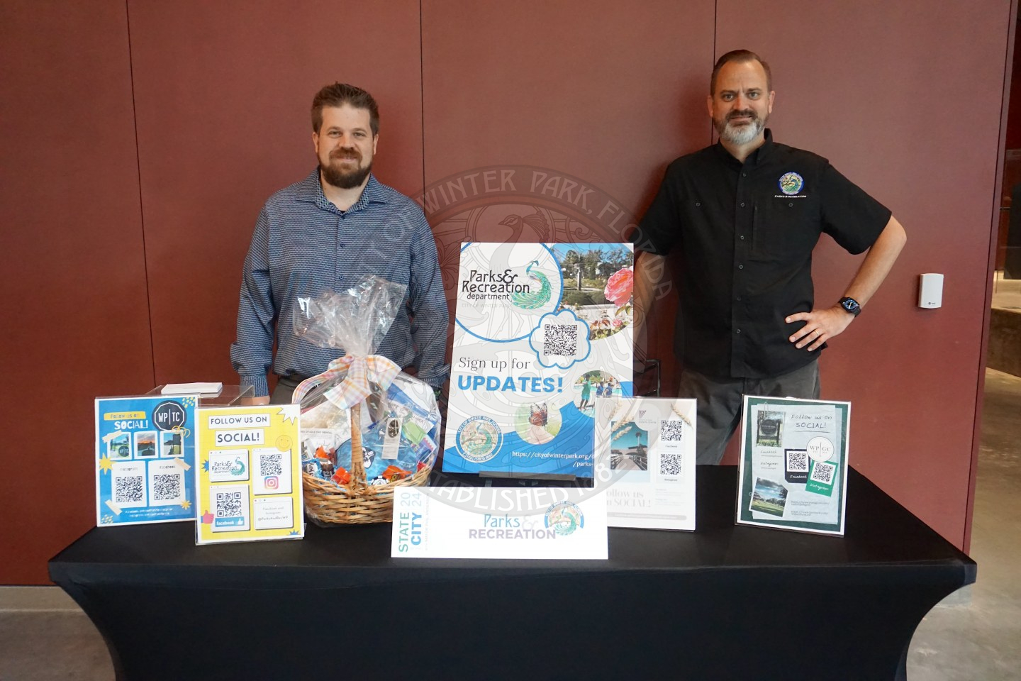 Two men standing behind a table with information about everyting parks and recreation related throughout the city.