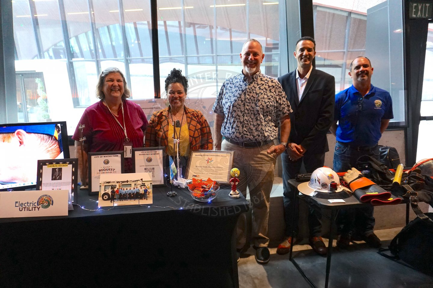 two women and three men standing behind a table with a bunch of information about the electric utility company.