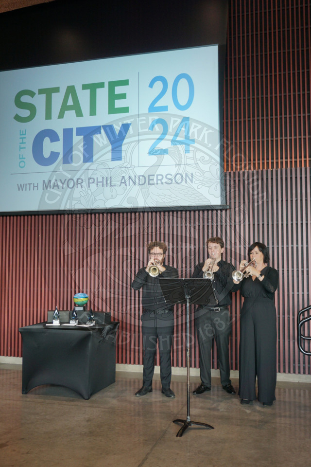 two men and one girl who are playing their trumpets standing in front of music stand and reading their music.