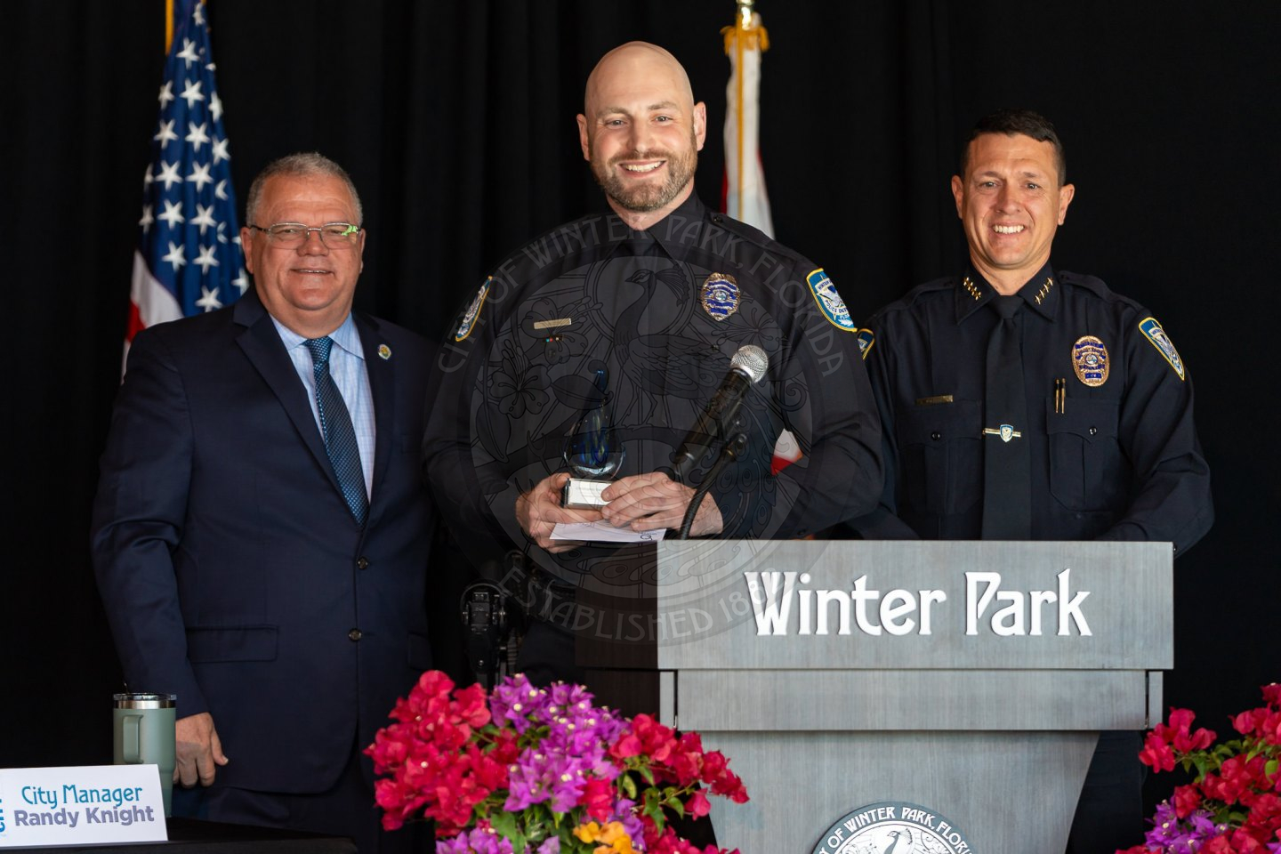 three males standing next to each other while the one in the middle is holding an award in his hands.