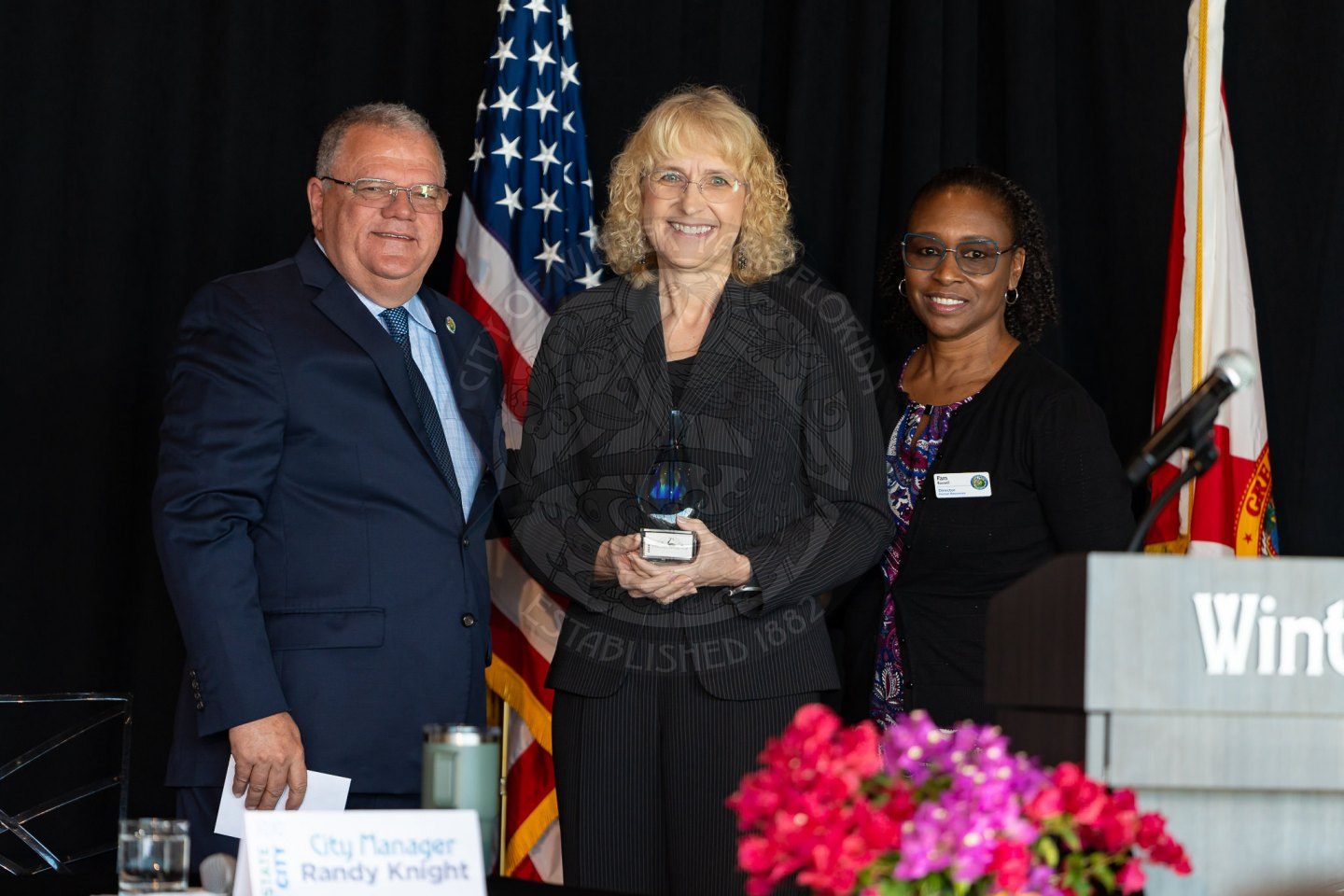 a male and two females standing next to each other with the one in the middle holding an award.