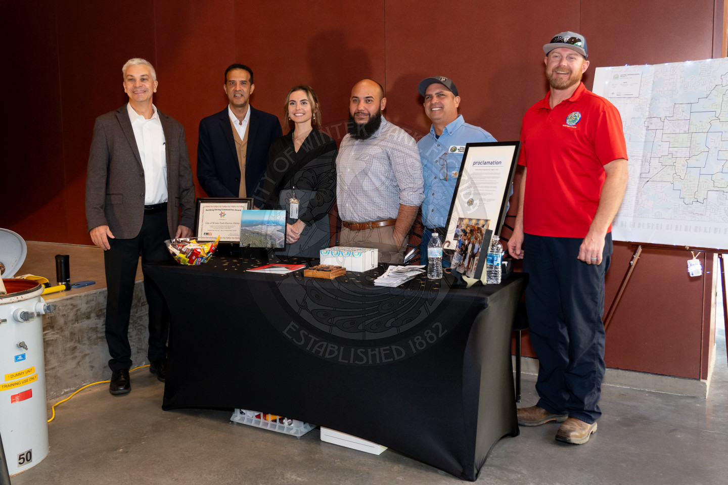 Group of people standing behind the table with the label of Electric utility. There is information and a bowl of candy on the table.
