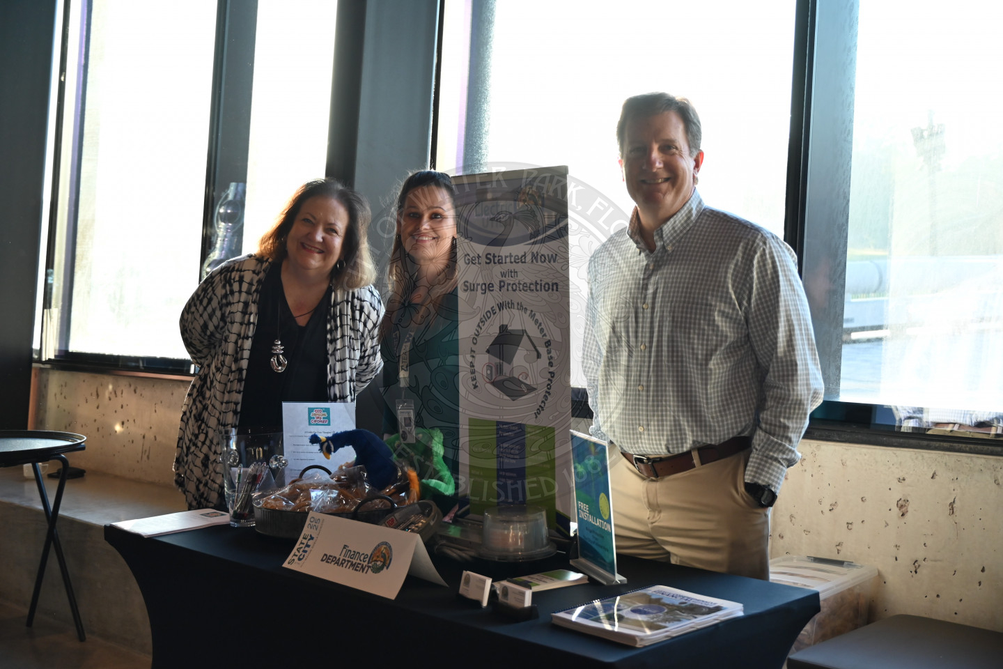two females and male standing behind the Finance table with information and cookies