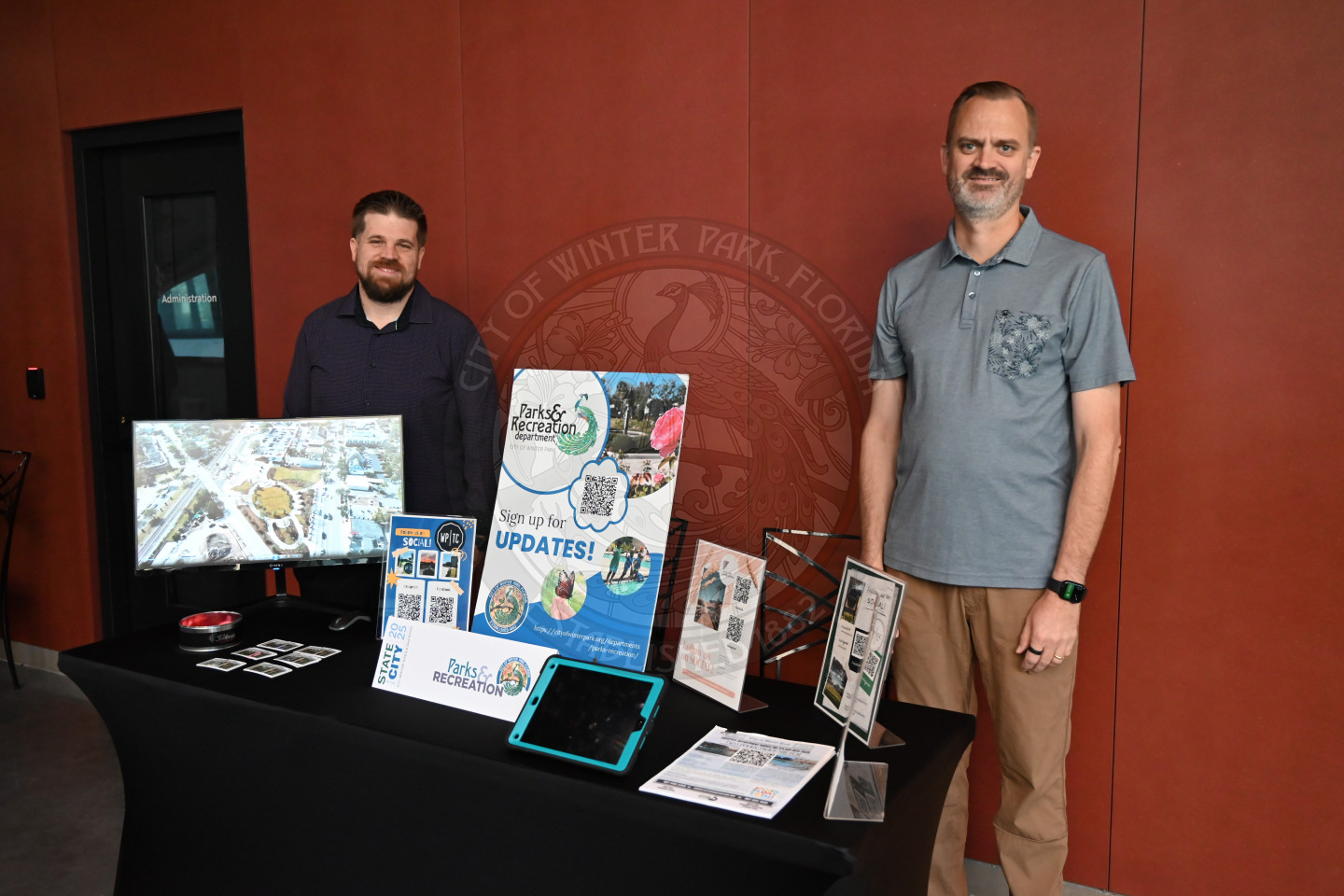 two men standing behind a desk with information about the parks &amp; recreation department.