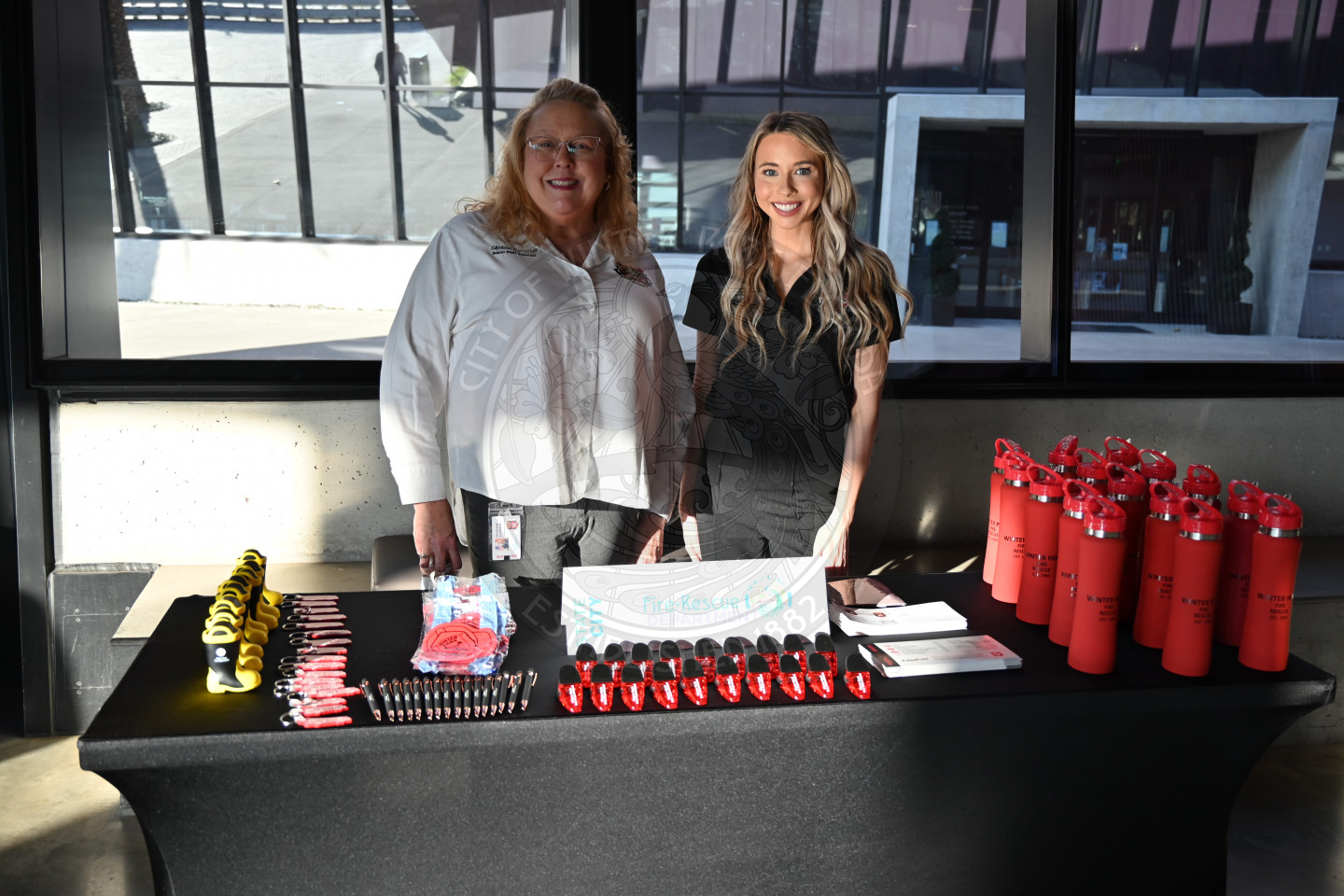 2 ladies standing behind the Fire-Rescue Department with fire sample items.