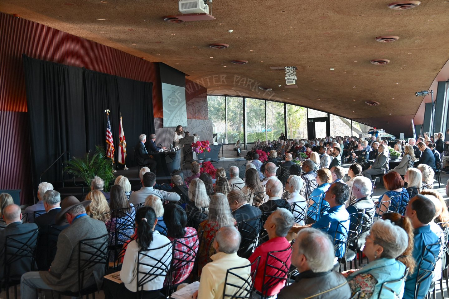 back view of attendees in seats looking at the stage while the mayor is presenting her speech.