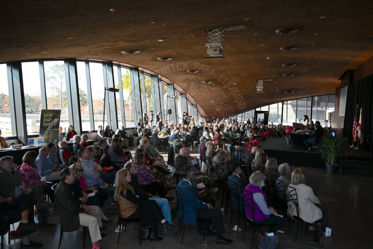people sitting in chairs and tables listening to the speakers on the stage.